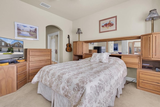 bedroom with light colored carpet, visible vents, and arched walkways