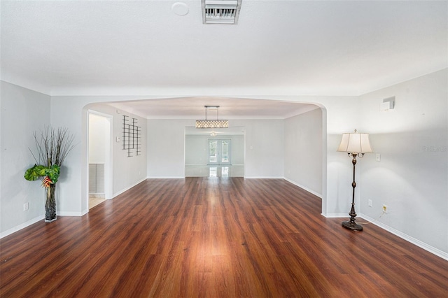 interior space featuring arched walkways, baseboards, wood finished floors, and visible vents