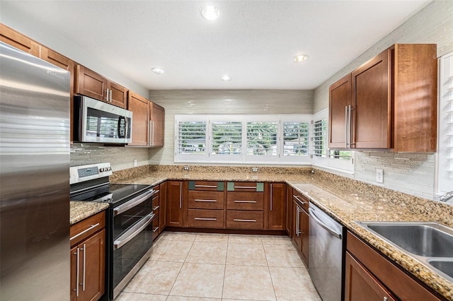 kitchen featuring appliances with stainless steel finishes, light stone counters, a sink, recessed lighting, and decorative backsplash