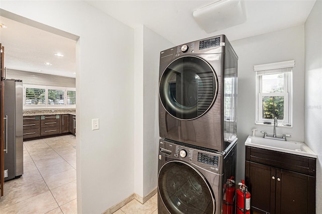 washroom with stacked washing maching and dryer, baseboards, light tile patterned flooring, and a sink
