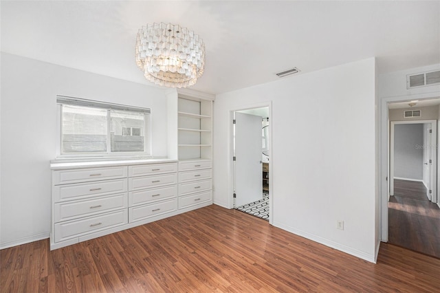 unfurnished bedroom with baseboards, visible vents, an inviting chandelier, and wood finished floors