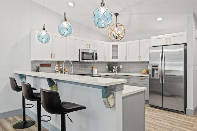 kitchen featuring white cabinets, a peninsula, stainless steel appliances, glass insert cabinets, and a breakfast bar area