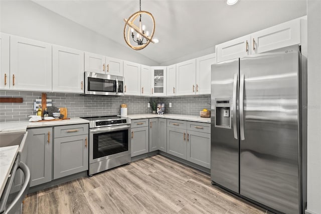 kitchen featuring vaulted ceiling, backsplash, light wood finished floors, appliances with stainless steel finishes, and gray cabinetry