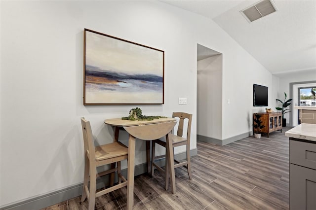 dining space featuring baseboards, visible vents, wood finished floors, and vaulted ceiling