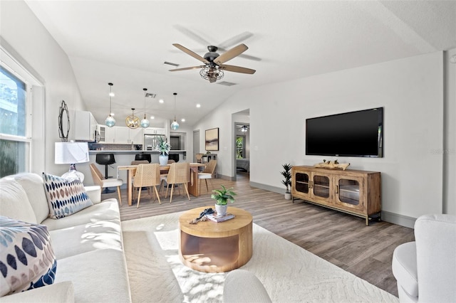 living area with lofted ceiling, baseboards, light wood-style floors, visible vents, and a ceiling fan