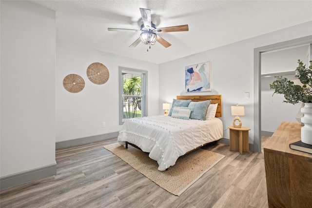 bedroom with ceiling fan, baseboards, light wood finished floors, and a textured ceiling