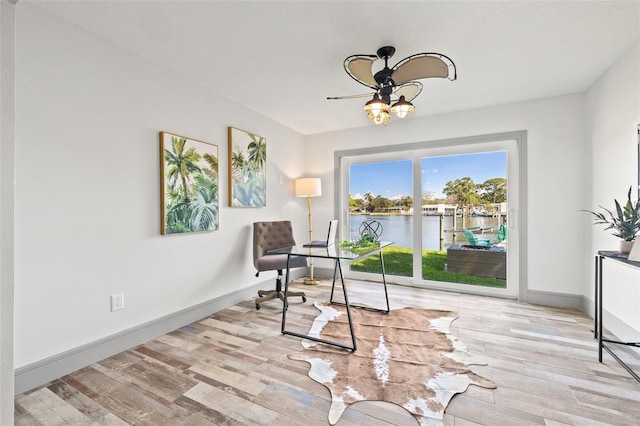 living area featuring baseboards, a water view, wood finished floors, and a ceiling fan