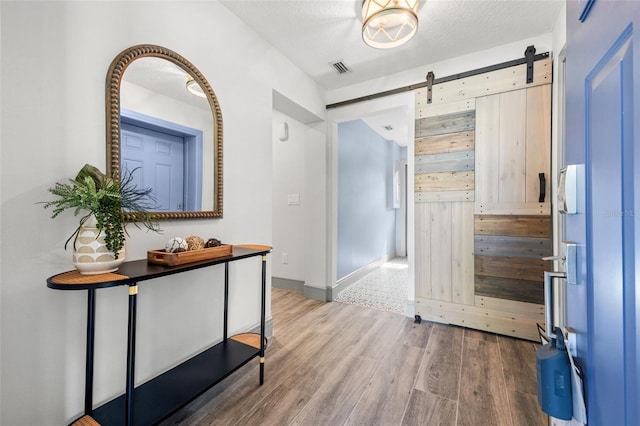 entrance foyer with visible vents, a textured ceiling, a barn door, and wood finished floors