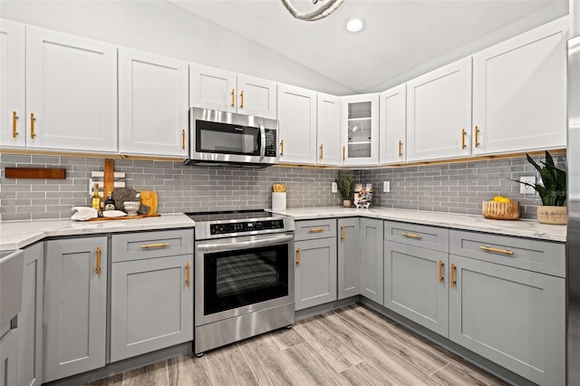 kitchen featuring tasteful backsplash, vaulted ceiling, gray cabinets, stainless steel appliances, and light wood-style flooring