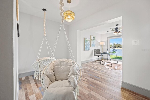living area with baseboards, wood finished floors, and ceiling fan