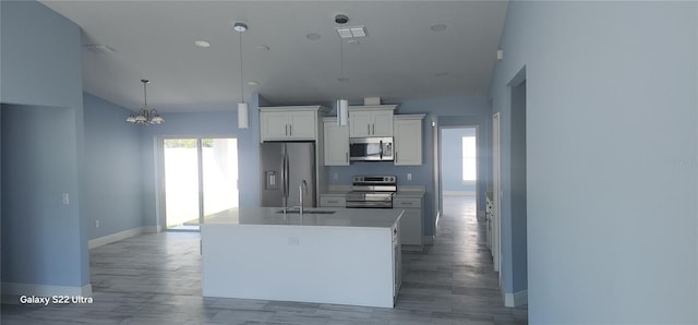 kitchen with stainless steel appliances, an inviting chandelier, a sink, a center island with sink, and white cabinetry