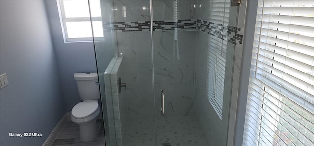 bathroom with toilet, baseboards, and a marble finish shower