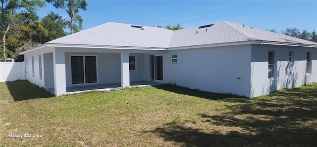 rear view of house with fence, a lawn, a shingled roof, and stucco siding
