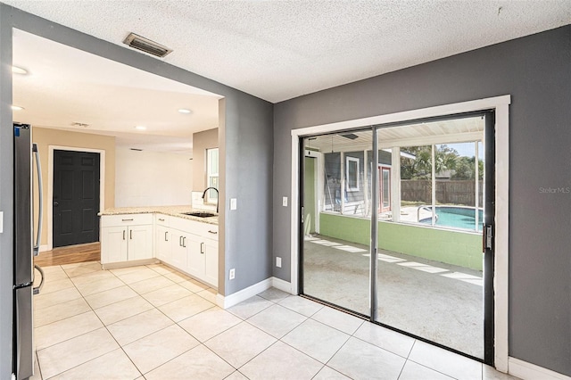 1366 Wexford Dr N, Palm Harbor, FL 34683 - kitchen featuring visible vents, a sink, white cabinetry, freestanding refrigerator, and light stone countertops