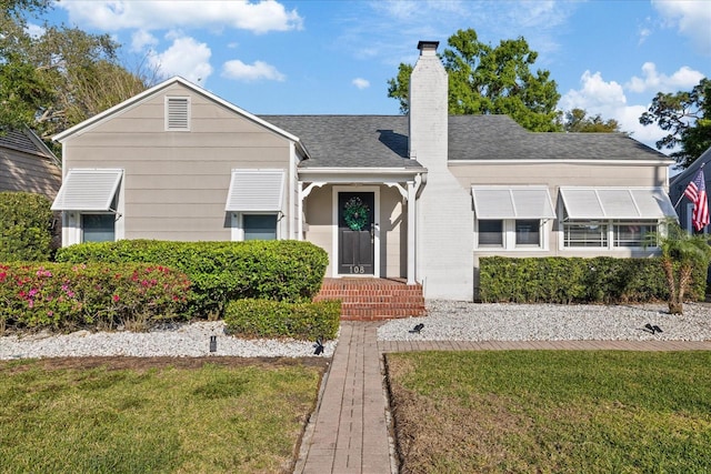 view of front of property featuring a chimney, a shingled roof, and a front yard