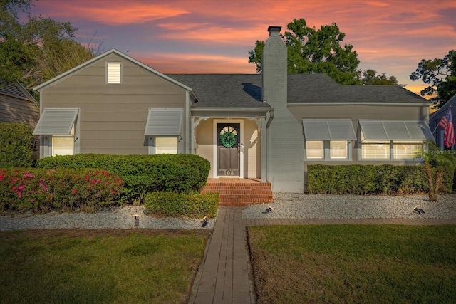 view of front of property featuring a lawn, a shingled roof, and a chimney