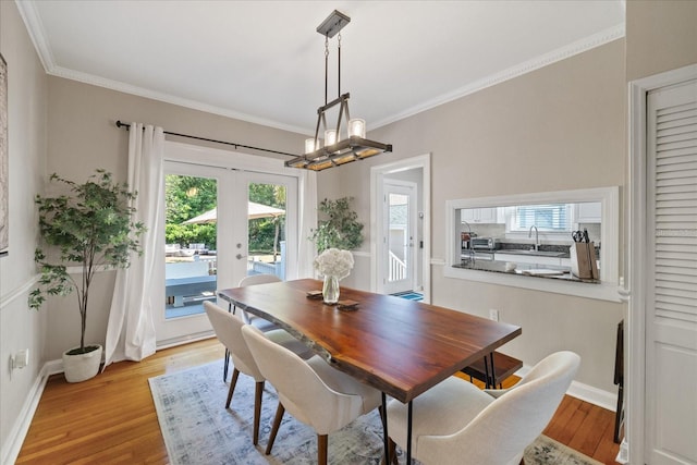 dining space with french doors, a chandelier, crown molding, and light wood finished floors