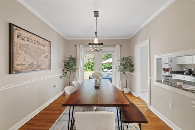 dining area with baseboards, a notable chandelier, crown molding, and light wood-style floors