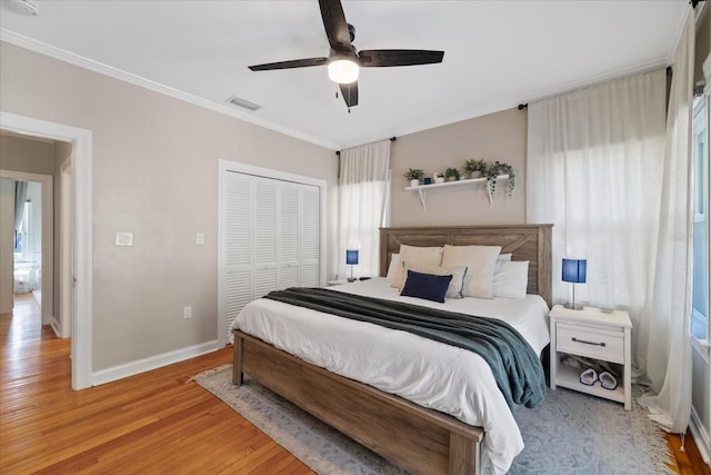 bedroom with ornamental molding, baseboards, light wood finished floors, visible vents, and a closet