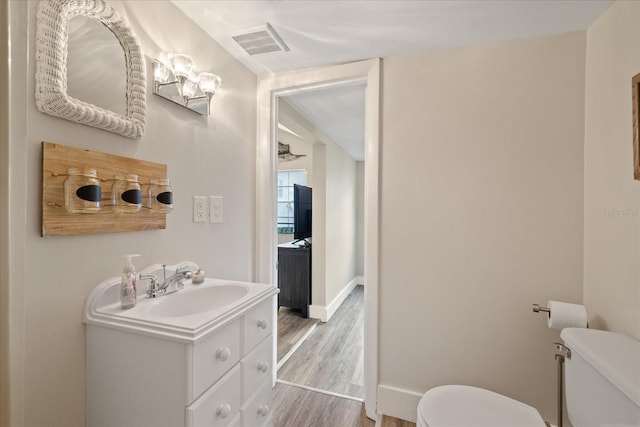 half bath featuring visible vents, baseboards, toilet, wood finished floors, and vanity