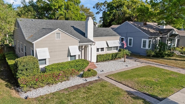 view of front facade with a chimney, a shingled roof, and a front lawn