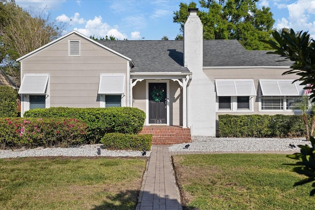 view of front facade with a front yard, a shingled roof, and a chimney