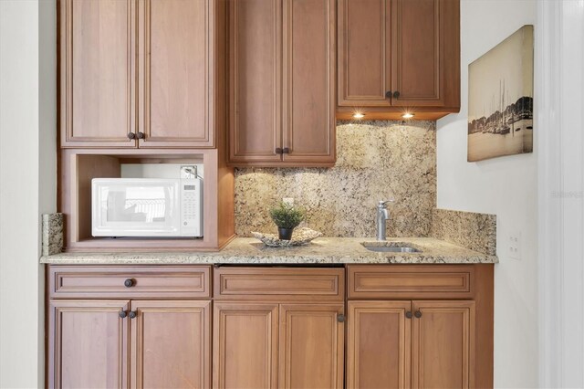 700 126th Ave, Treasure Island, FL 33706 - kitchen featuring light stone countertops, brown cabinets, tasteful backsplash, a sink, and white microwave