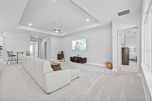 living area featuring light colored carpet, ceiling fan, a tray ceiling, and visible vents