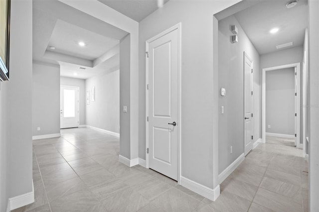 hallway with recessed lighting, a raised ceiling, baseboards, and light tile patterned flooring