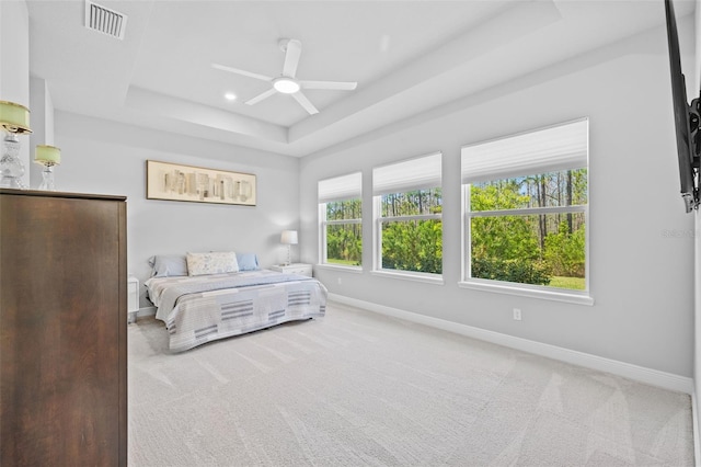 carpeted bedroom with a tray ceiling, visible vents, a ceiling fan, and baseboards
