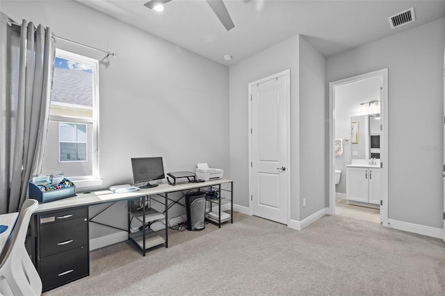 home office with a ceiling fan, a sink, light colored carpet, baseboards, and visible vents