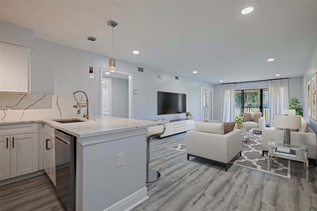 kitchen with a sink, light stone counters, open floor plan, white cabinets, and dishwasher