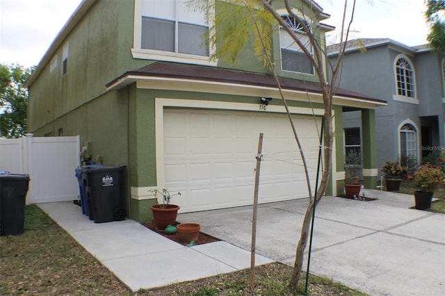 view of home's exterior with an attached garage, fence, driveway, and stucco siding