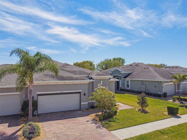 ranch-style home featuring stucco siding, a front lawn, decorative driveway, roof with shingles, and a garage