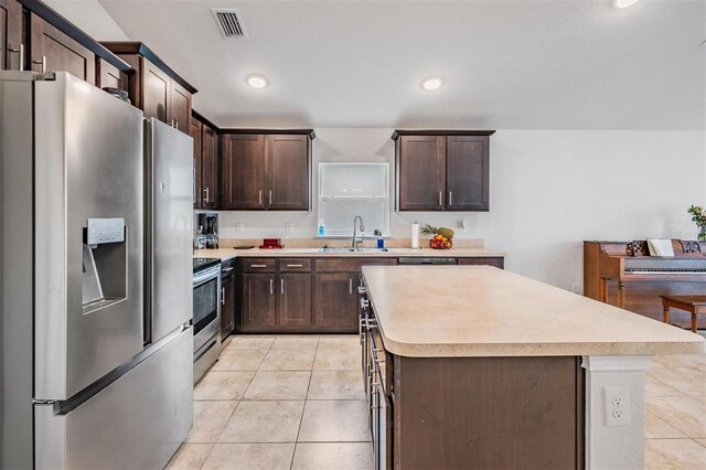 kitchen with dark brown cabinetry, light tile patterned flooring, appliances with stainless steel finishes, and a sink