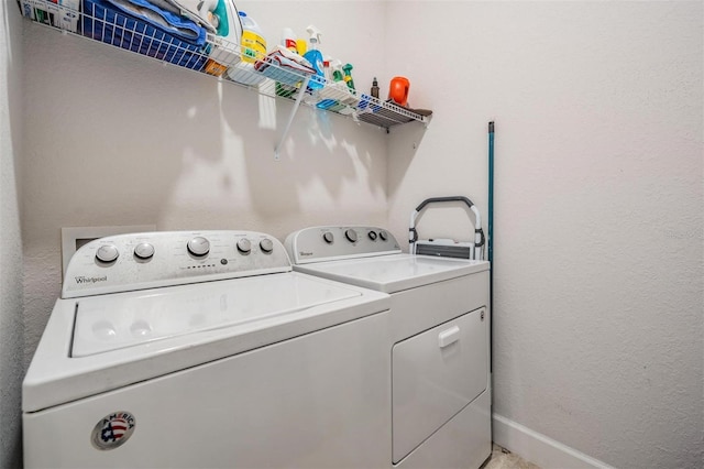 clothes washing area featuring washer and dryer, baseboards, laundry area, and a textured wall