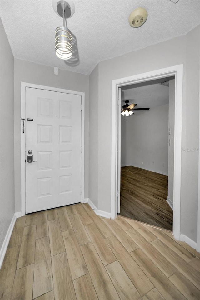 interior space with baseboards, a textured ceiling, and light wood finished floors