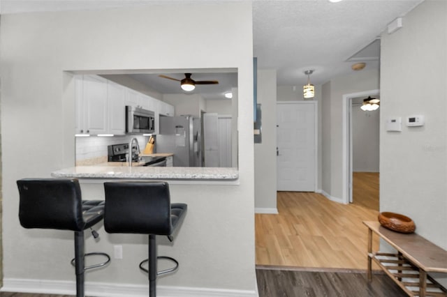 kitchen with decorative backsplash, appliances with stainless steel finishes, wood finished floors, white cabinetry, and a ceiling fan