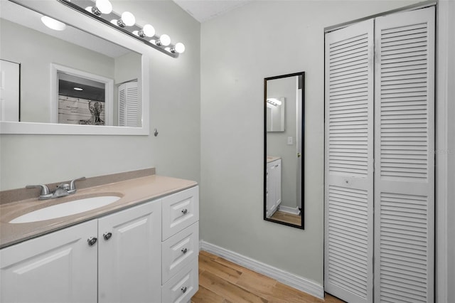 bathroom with a closet, vanity, baseboards, and wood finished floors