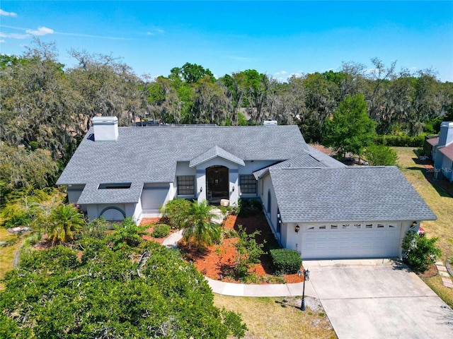 ranch-style home with stucco siding, roof with shingles, an attached garage, driveway, and a chimney