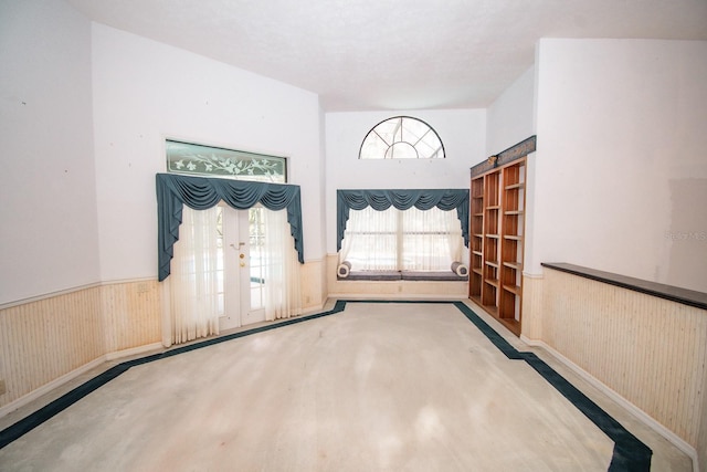 entryway featuring french doors, wood walls, carpet, and a wainscoted wall