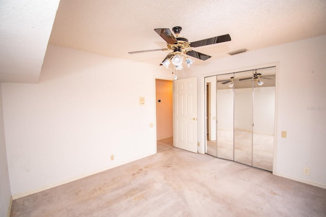 unfurnished bedroom with ceiling fan, a textured ceiling, carpet, visible vents, and a closet