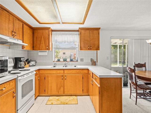 kitchen with under cabinet range hood, white range with electric stovetop, light countertops, a sink, and a peninsula
