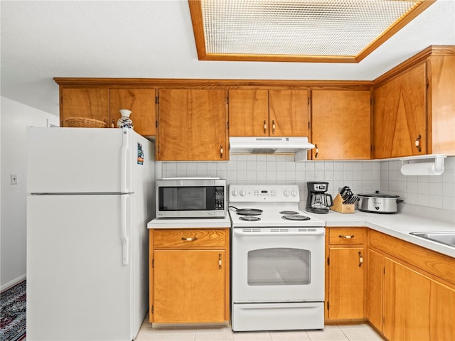 kitchen with tasteful backsplash, white appliances, brown cabinets, light countertops, and under cabinet range hood