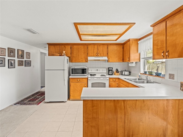 kitchen featuring brown cabinets, white appliances, light countertops, under cabinet range hood, and visible vents