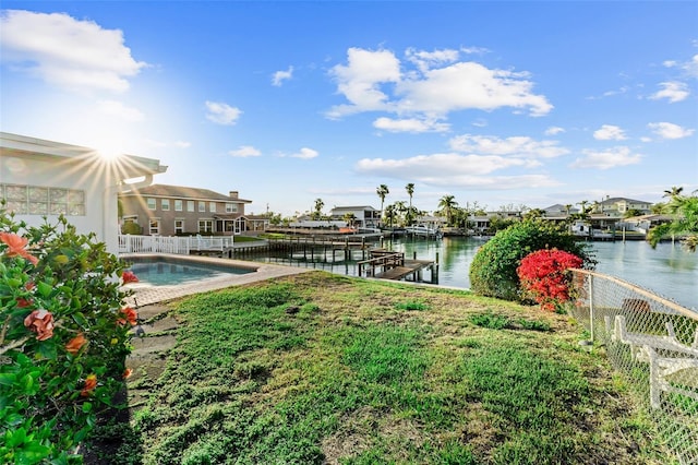view of yard with an outdoor pool, a dock, a water view, and fence