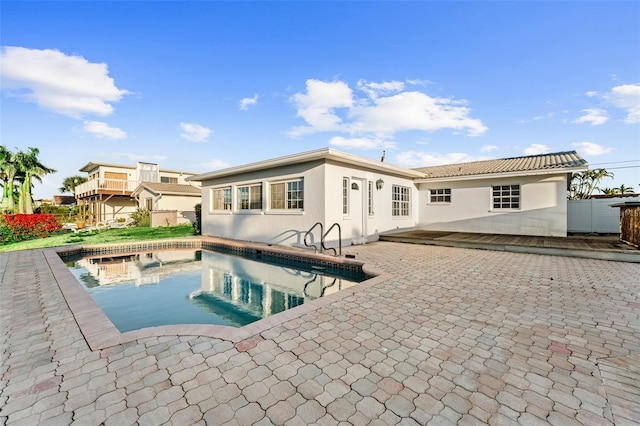 rear view of house with a fenced in pool, stucco siding, a patio, and fence