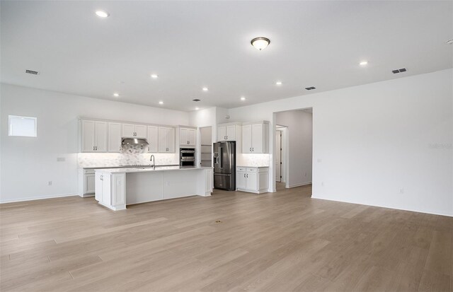 kitchen featuring backsplash, stainless steel double oven, open floor plan, under cabinet range hood, and high end fridge