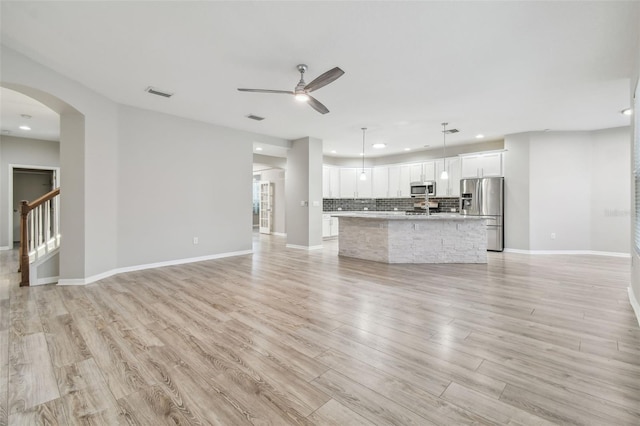 12304 Silton Peace Dr, Riverview, FL 33579 - unfurnished living room featuring visible vents, arched walkways, light wood finished floors, baseboards, and ceiling fan