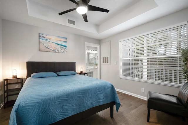 bedroom featuring a tray ceiling, baseboards, visible vents, and wood finished floors